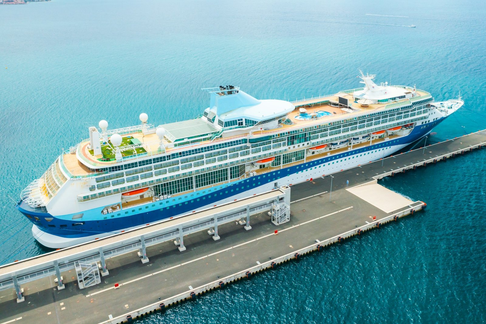 Aerial view of a luxury cruise ship or linear with a swimming pool and golf field on the roof moored